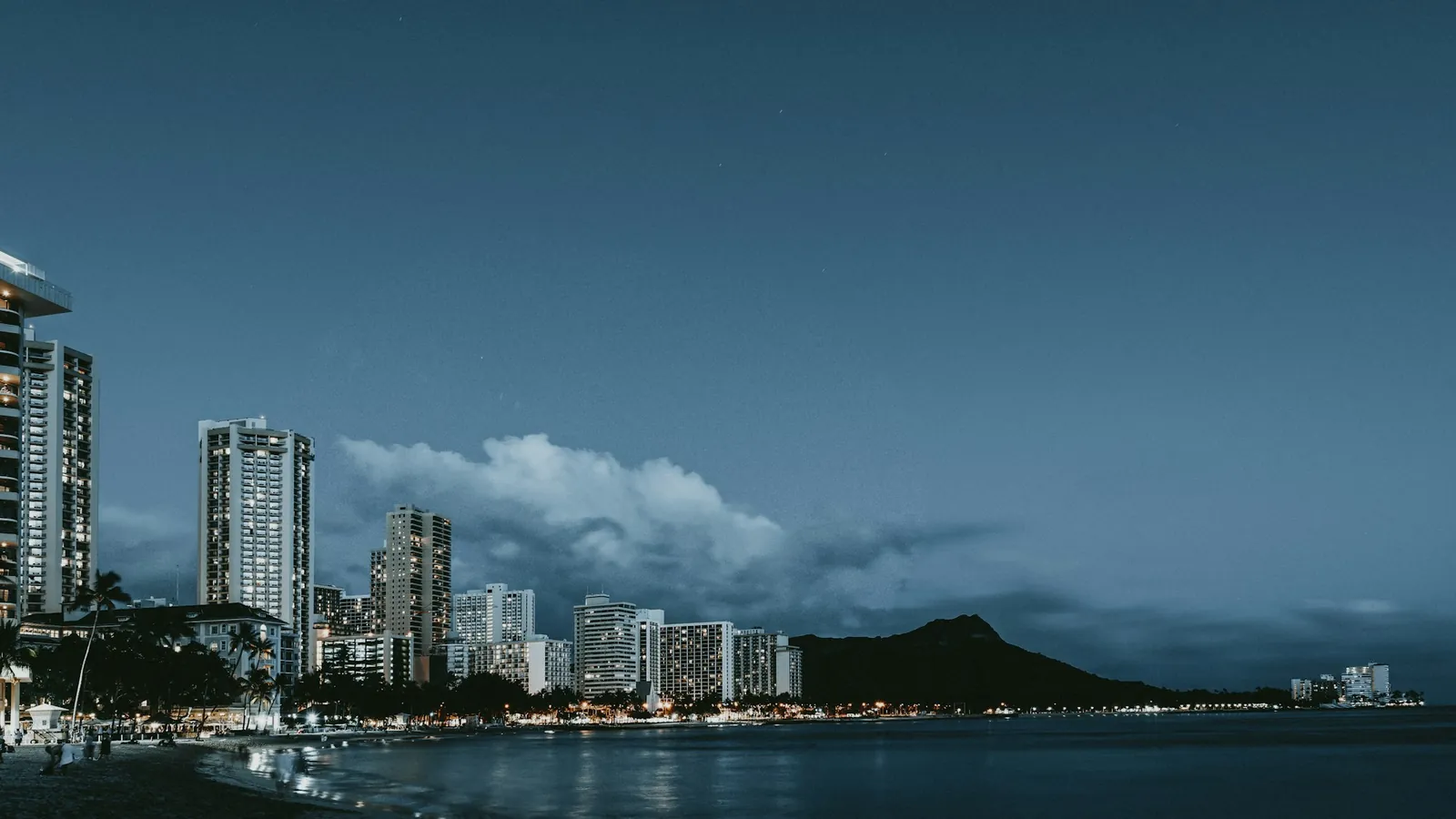 Waikīkī high-rise buildings along the shore with Diamond Head at dusk
