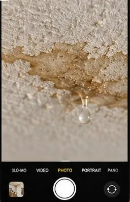 Phone camera close-up of a wet ceiling stain with a water droplet