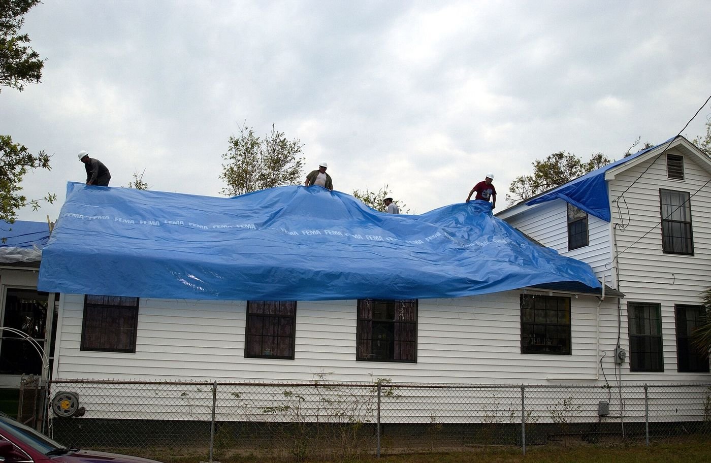A crew stretches a blue tarp over a storm-damaged roof to stop further water damage