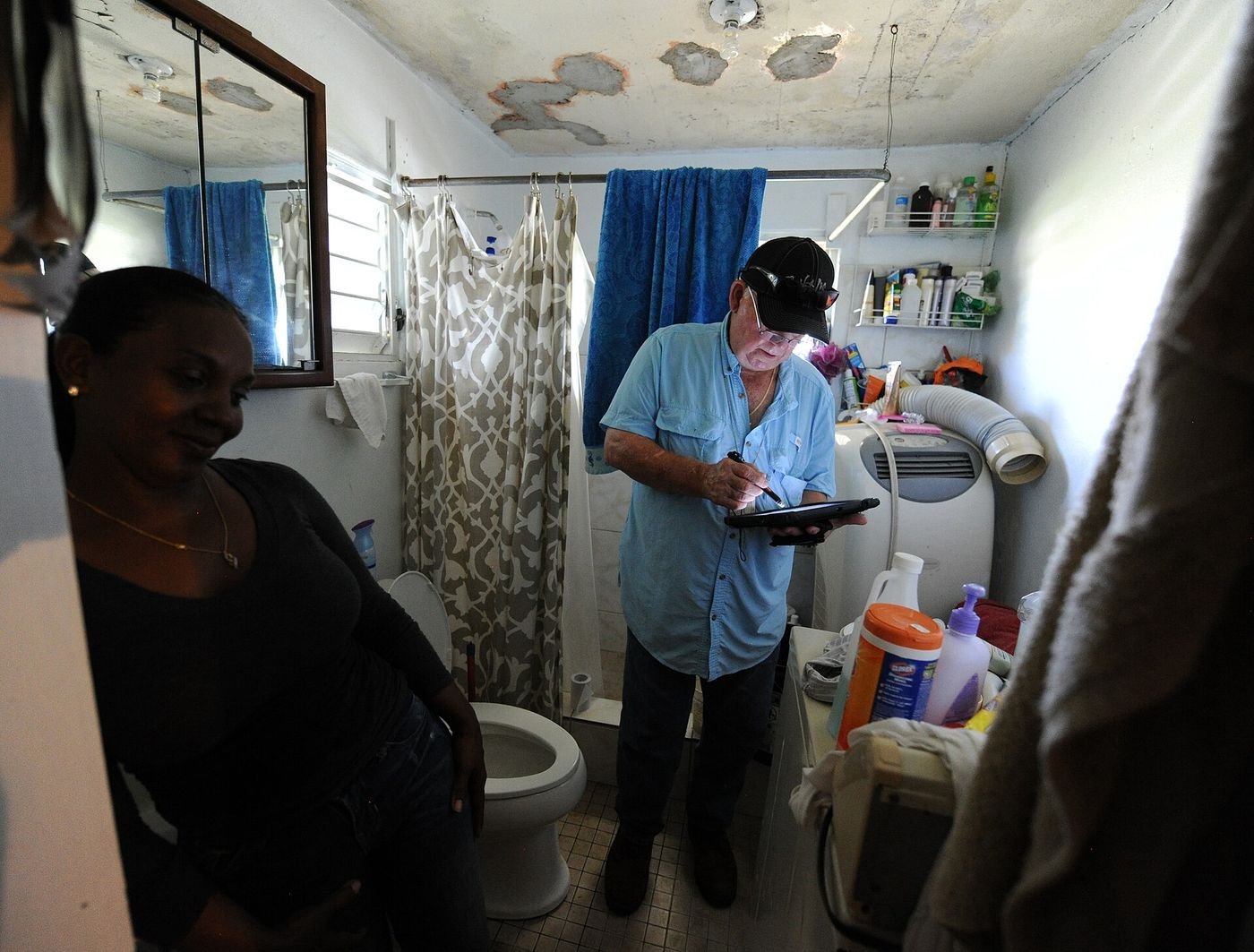 A housing inspector documents water-damaged, peeling ceiling paint in a storm-damaged bathroom