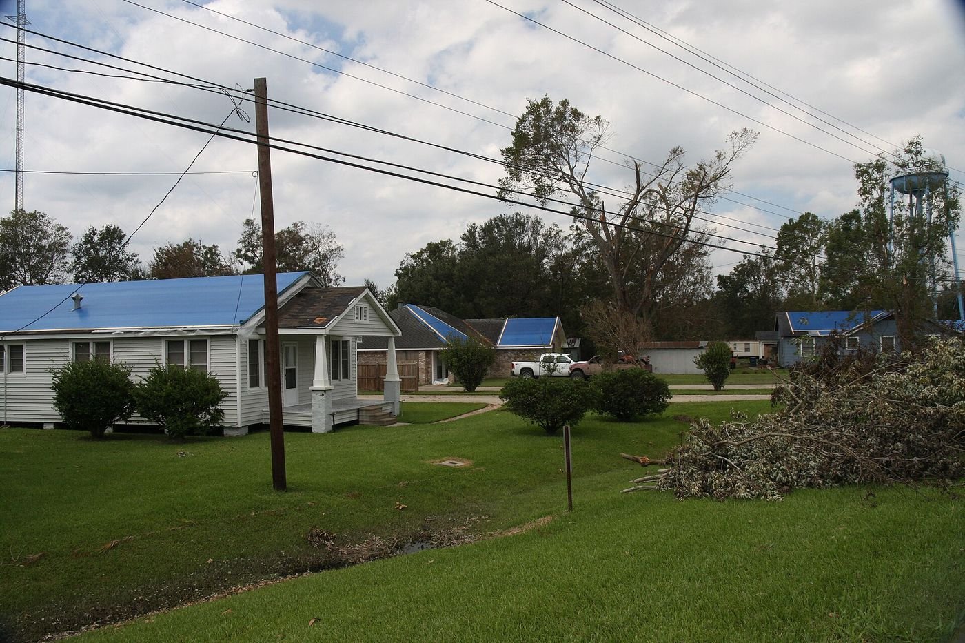 A neighborhood street of homes with blue tarps on damaged roofs and piles of storm debris
