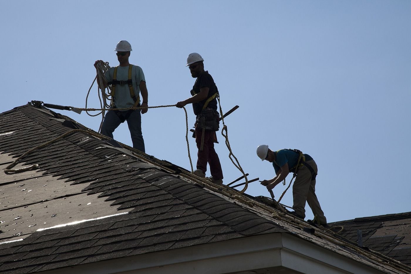 A roofing crew works on a storm-damaged shingle roof