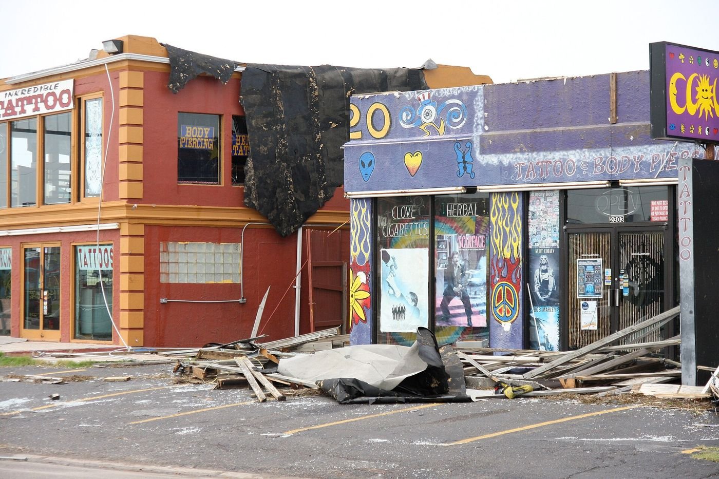 Storefronts with torn roofs and debris in the parking lot after a hurricane
